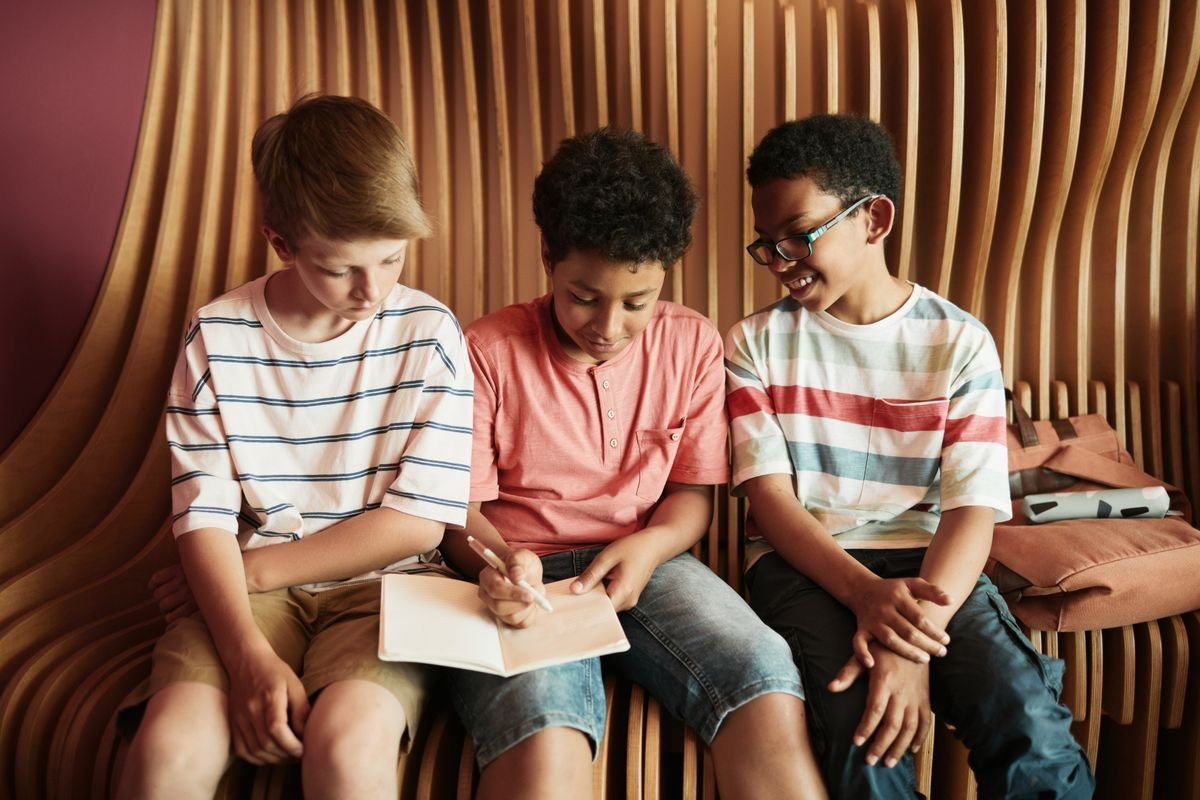 Three learners sharing ideas over a notebook